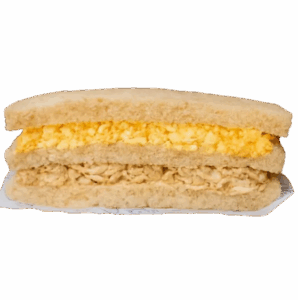 Sanduíche de pão de forma com recheio farto de frango desfiado e ovos cozidos ralados, servido em um prato branco.